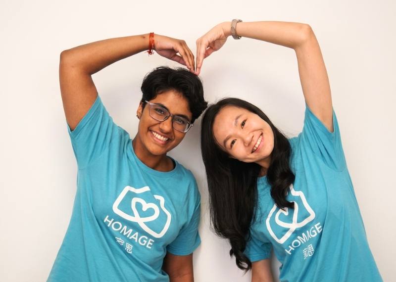 Two Homage team members in branded t-shirts making a heart shape with their arms