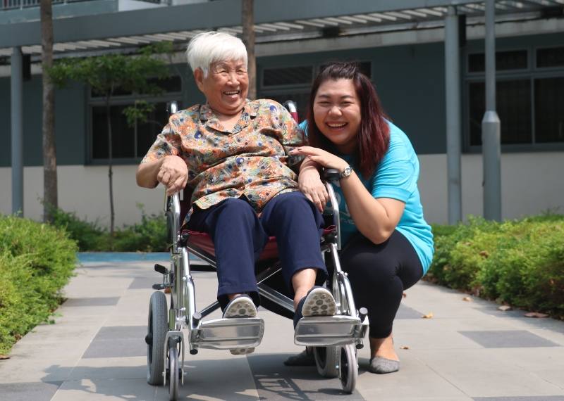 A care worker outdoors with a client in a wheelchair, both laughing